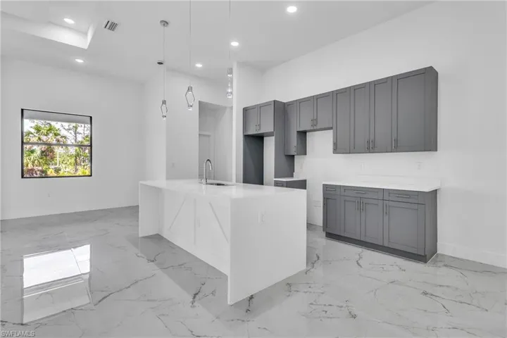 Kitchen featuring recessed lighting, gray cabinetry, light stone countertops, a center island with sink, and hanging light fixtures