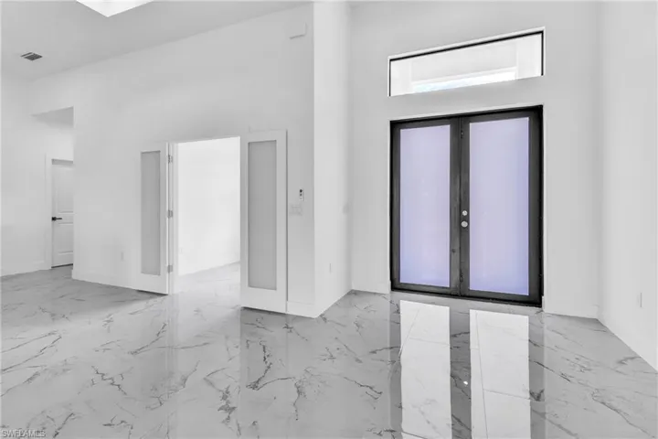 Foyer entrance featuring a towering ceiling, french doors, and light marble finish floors