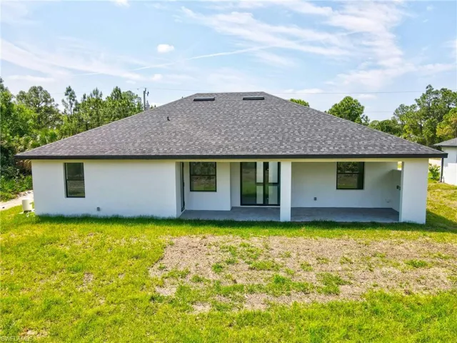 Rear view of property featuring stucco siding, a patio, a lawn, and a shingled roof