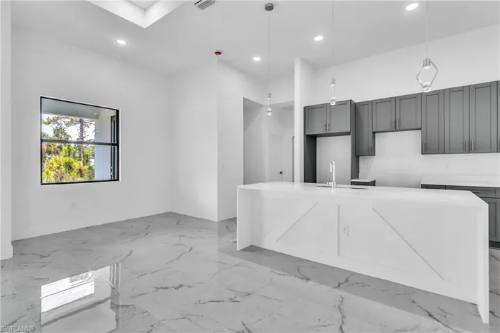 Kitchen with light marble finish floors, a center island with sink, recessed lighting, light stone counters, and decorative light fixtures