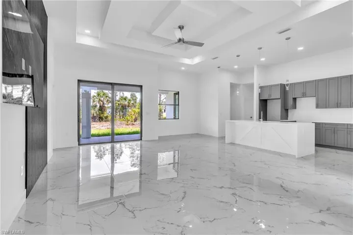 Unfurnished living room with a tray ceiling, light marble finish flooring, a ceiling fan, and recessed lighting