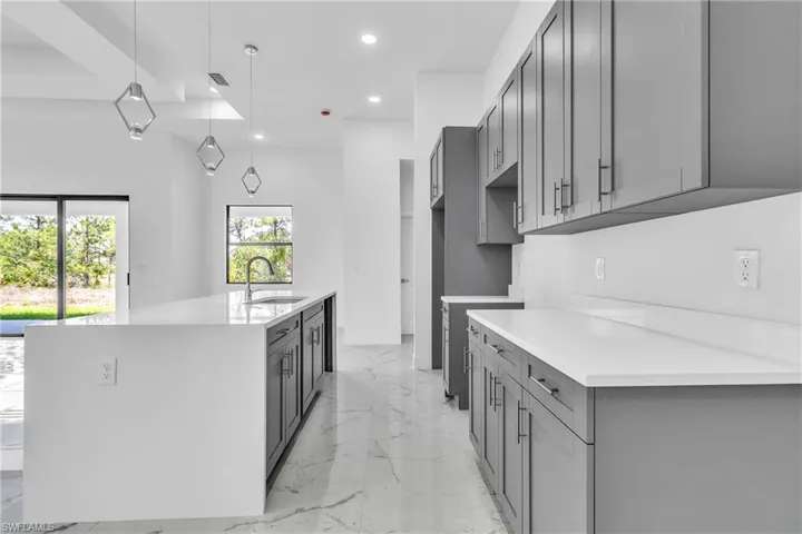 Kitchen featuring recessed lighting, hanging light fixtures, light marble finish floors, light stone counters, and gray cabinetry