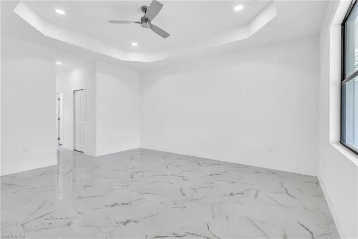 Unfurnished room featuring a tray ceiling, recessed lighting, light marble finish floors, and ceiling fan