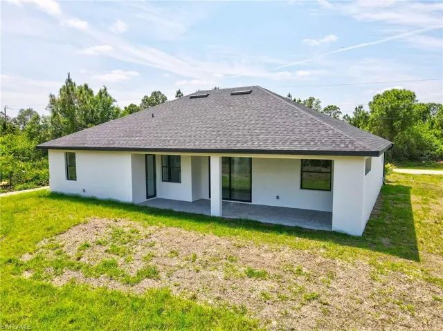 Rear view of house featuring a lawn, stucco siding, a patio, and roof with shingles