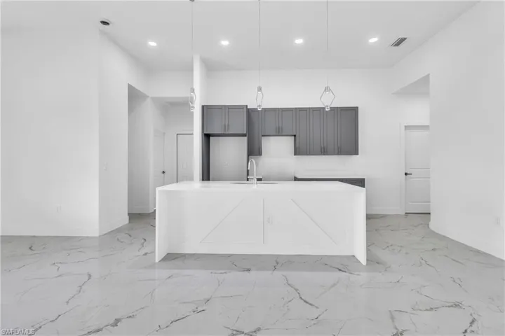 Kitchen with a kitchen island with sink, light stone counters, recessed lighting, pendant lighting, and light marble finish flooring