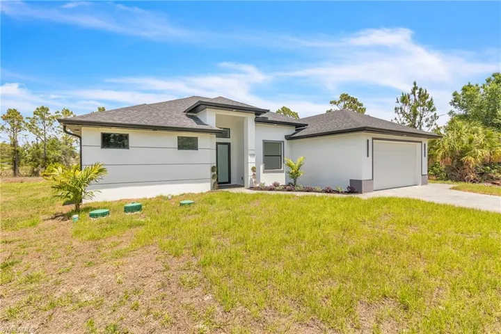 Prairie-style home featuring an attached garage, a front yard, driveway, and stucco siding