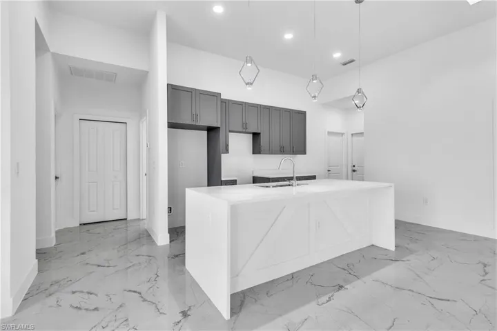 Kitchen featuring hanging light fixtures, light stone counters, a kitchen island with sink, light marble finish flooring, and recessed lighting