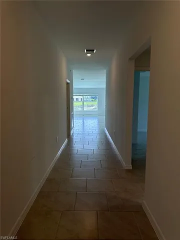 Spacious hallway featuring large format tile flooring, contemporary flush mount lighting, and white baseboards