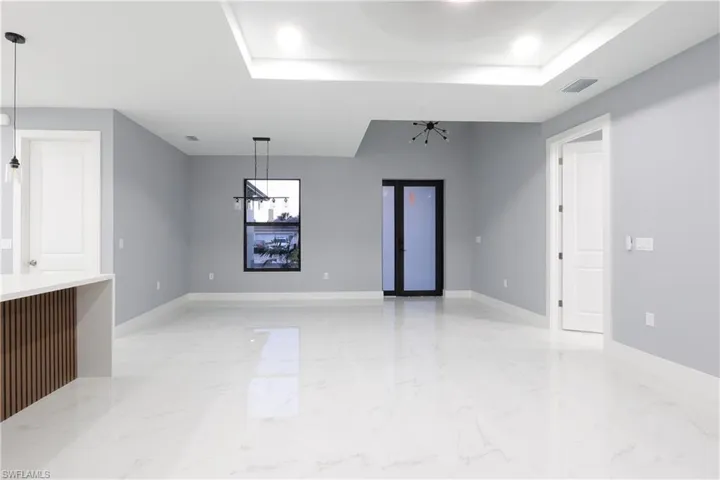 Unfurnished living room with a chandelier, a raised ceiling, light marble finish floors, and recessed lighting