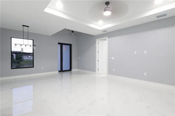 Spare room featuring a chandelier, light marble finish flooring, a tray ceiling, and ceiling fan