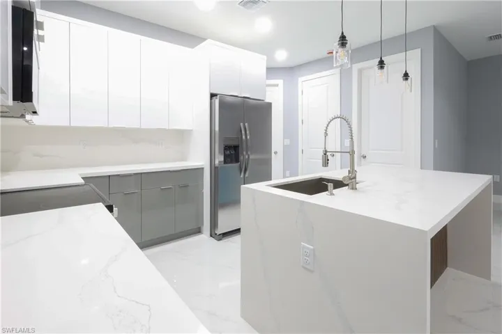Kitchen featuring gray cabinetry, stainless steel fridge with ice dispenser, light marble finish floors, white cabinets, and modern cabinets
