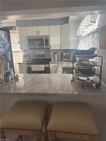 Kitchen with white cabinets, stainless steel appliances, light stone counters, and a breakfast bar area