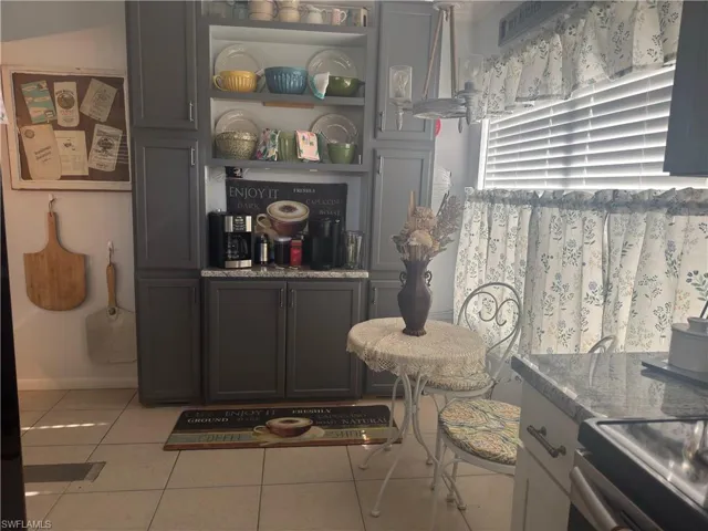 Kitchen with stainless steel range with electric stovetop, dark stone counters, light tile patterned floors, open shelves, and gray cabinets