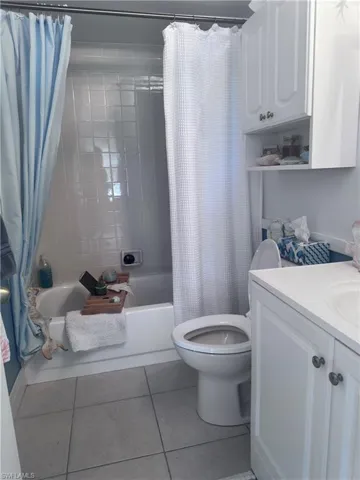 Full bathroom with shower / bath combo with shower curtain, light tile patterned floors, and vanity