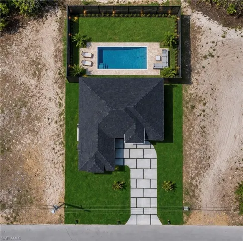 Manicured rear yard featuring a rectangular swimming pool with surrounding patio, lush green lawn, and privacy fencing