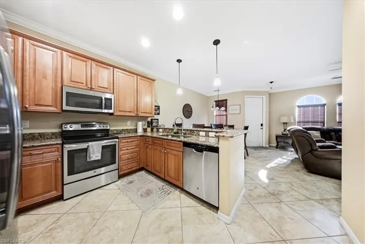 Kitchen featuring crown molding, appliances with stainless steel finishes, dark stone counters, decorative light fixtures, and a peninsula