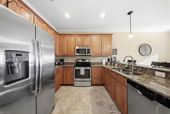 Kitchen featuring appliances with stainless steel finishes, dark stone countertops, brown cabinets, pendant lighting, and recessed lighting