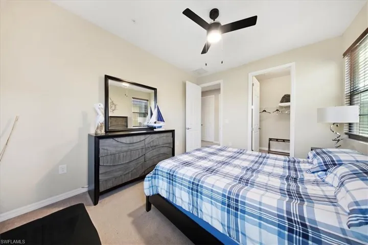 Bedroom with light colored carpet, a spacious closet, and ceiling fan