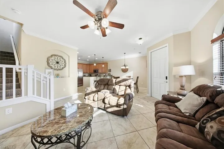Living area featuring stairs, ornamental molding, light tile patterned floors, and ceiling fan