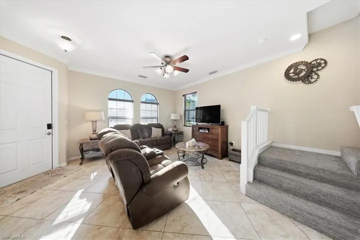 Living area featuring a ceiling fan, ornamental molding, stairs, and light tile patterned flooring