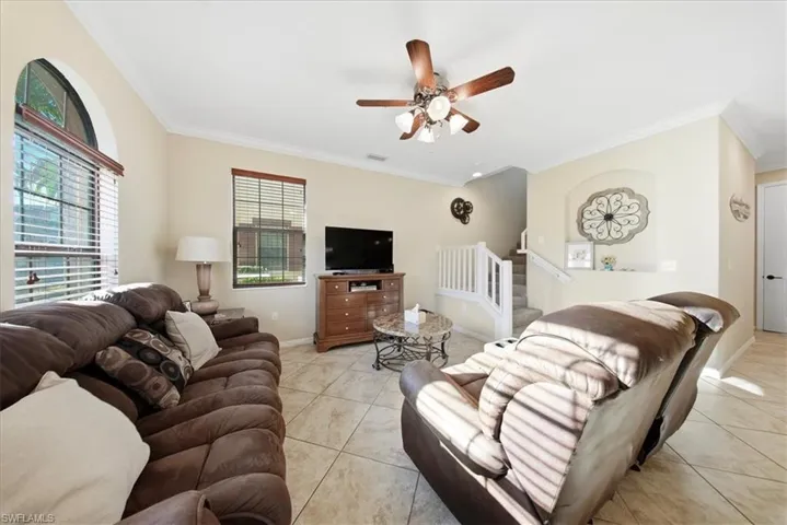 Living area featuring crown molding, stairway, ceiling fan, and light tile patterned flooring