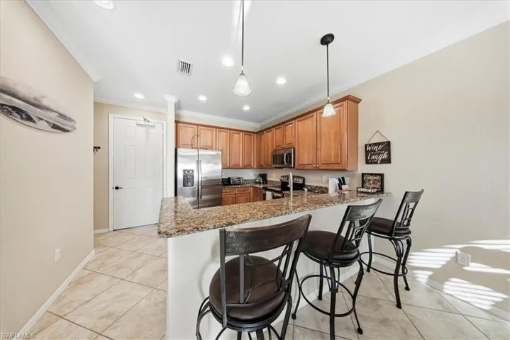 Kitchen featuring appliances with stainless steel finishes, dark stone counters, light tile patterned floors, decorative light fixtures, and ornamental molding