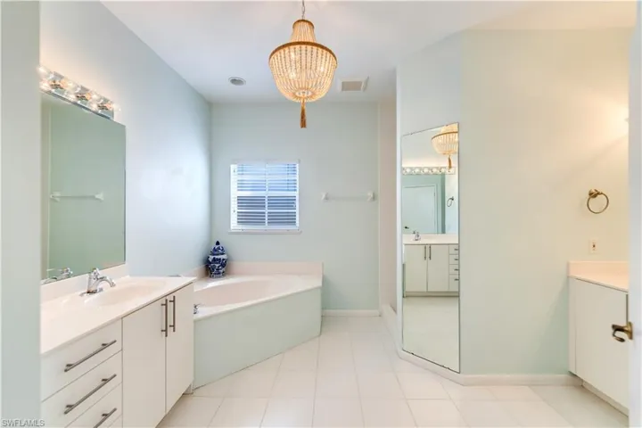Bathroom with tile floors, a washtub, a chandelier, 2 vanities and linen closet