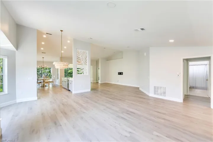 Unfurnished living room featuring an Anthropolgie chandelier, light wood-type flooring, and vaulted ceiling