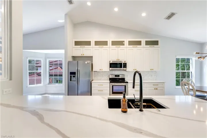 Kitchen featuring appliances with stainless steel finishes, new white cabinetry, light quartz countertops, and vaulted ceiling
