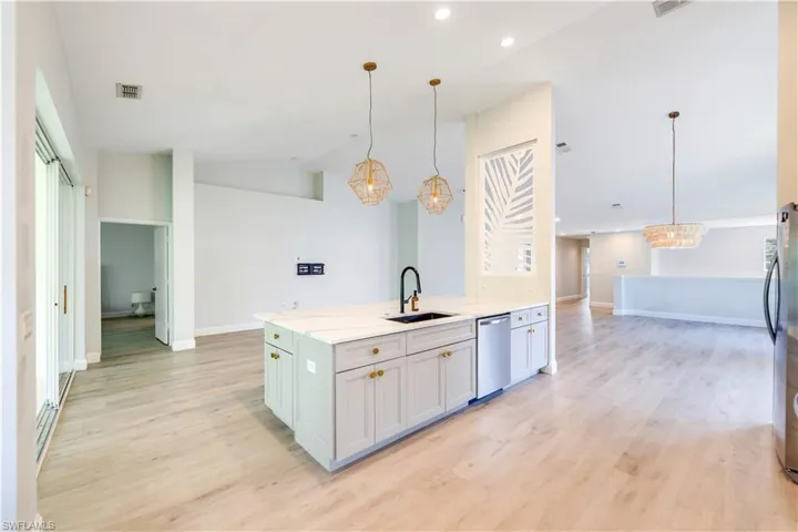 Kitchen featuring light beachy LVP wood-style flooring, new dishwasher, white and soft gray cabinetry, undermount sink, and pendant lighting
