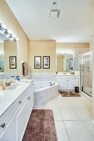 Full bath featuring a shower stall, two vanities, a garden tub, and light tile patterned floors