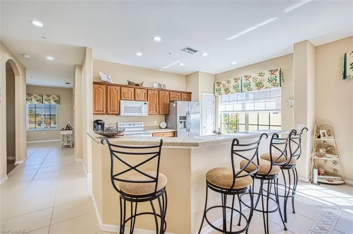 Kitchen featuring a breakfast bar area, light tile patterned floors, white appliances, arched walkways, and recessed lighting