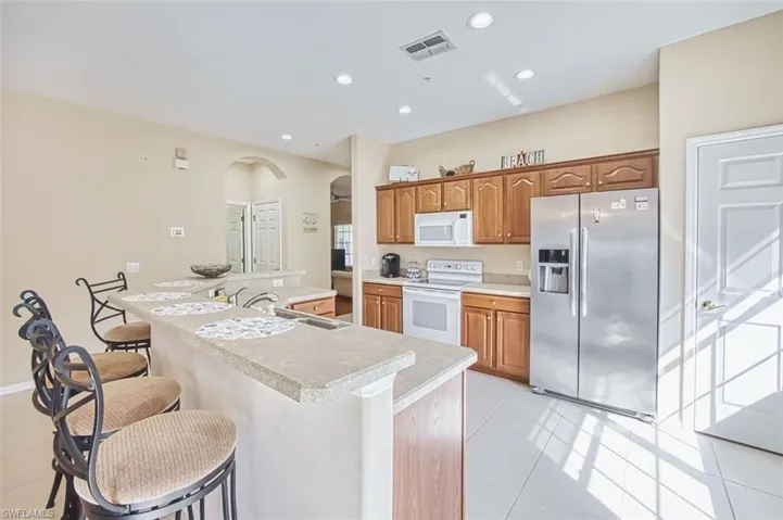 Kitchen featuring arched walkways, white appliances, an island with sink, light countertops, and a kitchen breakfast bar