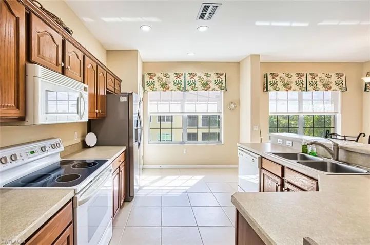 Kitchen featuring white appliances, light countertops, wood finish cabinets, light tile patterned floors, and recessed lighting