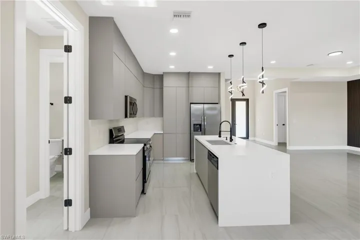 Kitchen featuring gray cabinetry, stainless steel appliances, modern cabinets, decorative light fixtures, and a center island with sink