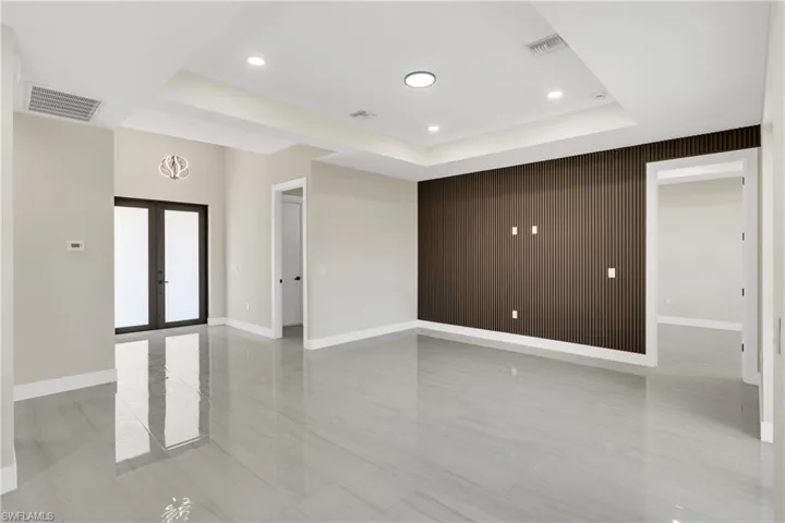 Empty room featuring french doors, an accent wall, wood walls, recessed lighting, and a raised ceiling