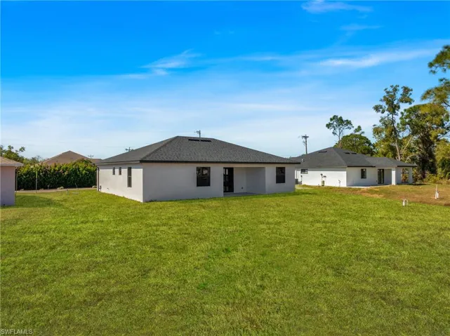 Rear view of property with a lawn, a patio area, and stucco siding