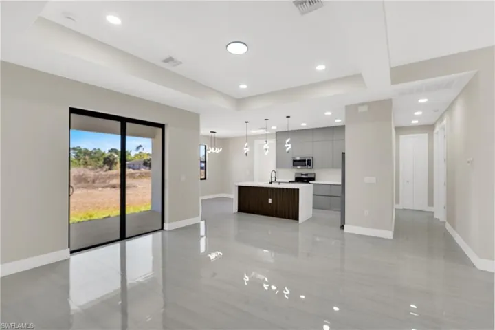 Kitchen with open floor plan, modern cabinets, a tray ceiling, an island with sink, and stainless steel microwave