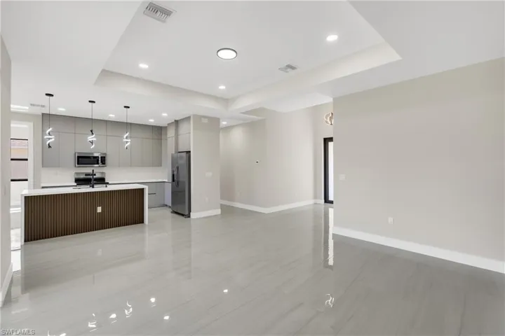 Kitchen featuring open floor plan, a kitchen island with sink, modern cabinets, gray cabinets, and decorative light fixtures