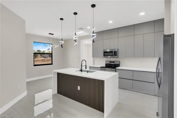 Kitchen with gray cabinets, modern cabinets, stainless steel appliances, an island with sink, and decorative light fixtures