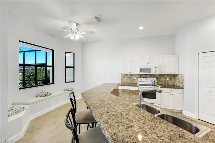 Kitchen with white cabinetry, white appliances, a kitchen breakfast bar, decorative backsplash, and recessed lighting