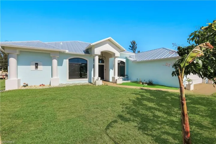 View of front facade with a front yard, an attached garage, stucco siding, and a new metal roof
