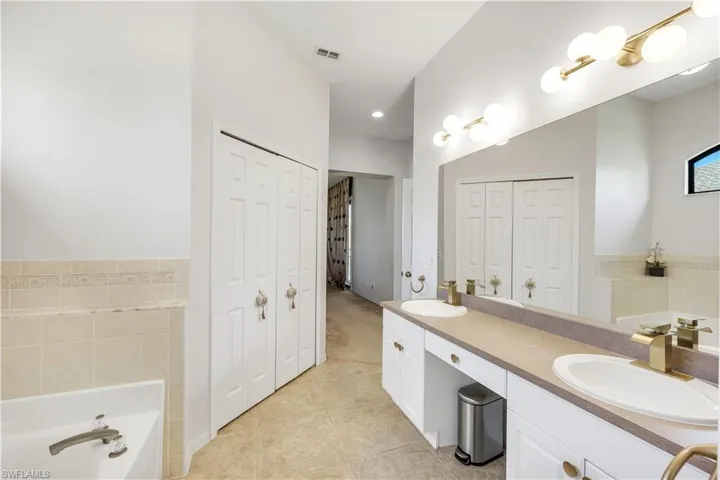 Master bath featuring a bath, a closet, double vanity, light tile patterned floors, and tile walls