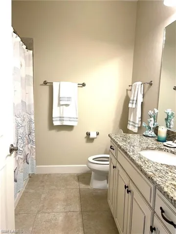 Full bath featuring vanity, toilet, a shower with shower curtain, tile patterned floors, and baseboards