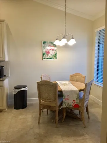 Dining area with light tile patterned floors, a notable chandelier, baseboards, and crown molding