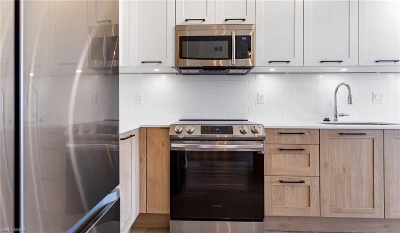 Kitchen with stainless steel appliances, backsplash, light stone countertops, and white cabinetry