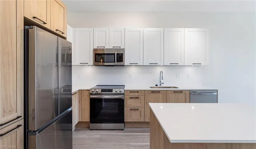 Kitchen featuring appliances with stainless steel finishes, tasteful backsplash, light wood finished floors, and light brown cabinetry
