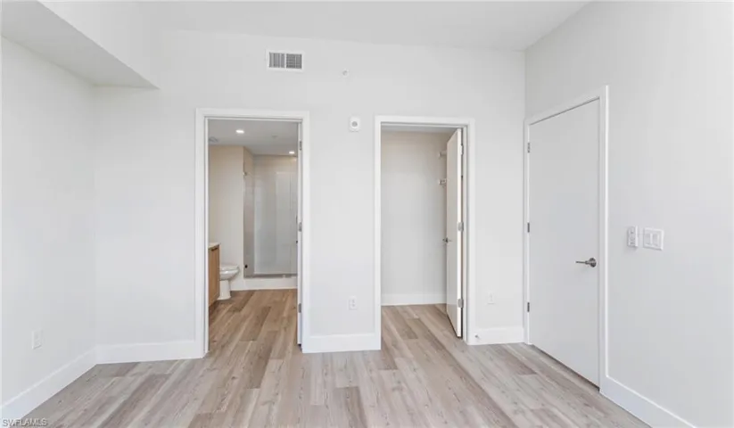 Unfurnished bedroom with a spacious closet, light wood-style flooring, and connected bathroom