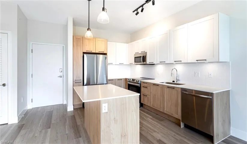 Kitchen featuring light brown cabinets, appliances with stainless steel finishes, a kitchen island, hanging light fixtures, and light wood-style flooring