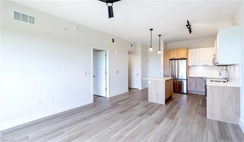 Kitchen featuring decorative backsplash, freestanding refrigerator, light brown cabinetry, a center island, and hanging light fixtures